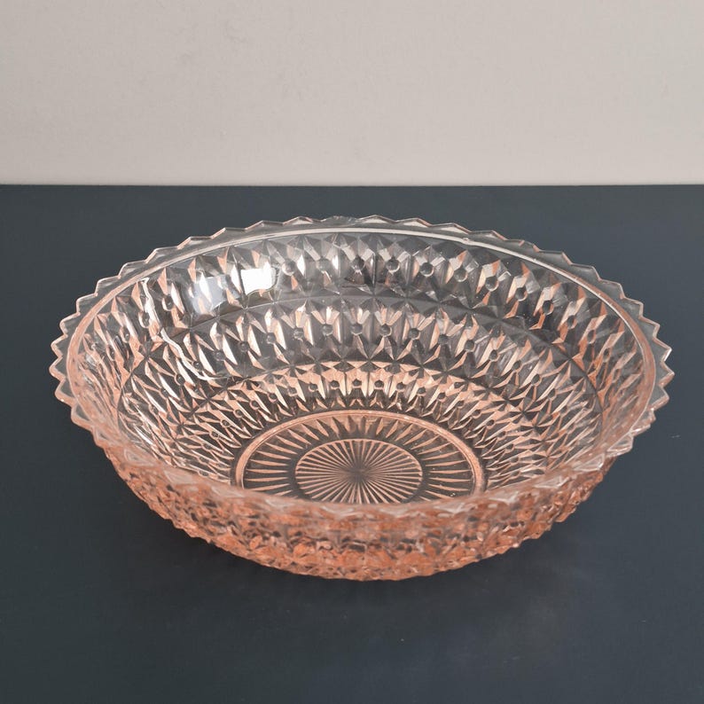 K&ouml;nnte beinhalten: Eine klare, rosa get&ouml;nte Glasschale mit Rautenmuster und gewelltem Rand. Die Schale hat ein kreisf&ouml;rmiges Design in der Mitte. Die Schale wird wahrscheinlich zum Servieren von Speisen oder als dekoratives St&uuml;ck verwendet.