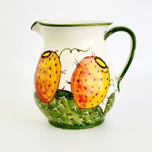 May include: A white ceramic pitcher with a green handle and rim. The pitcher is decorated with two yellow and orange prickly pear cactus fruits and green cactus leaves. The pitcher is a decorative item for the kitchen.