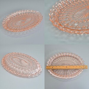 K&ouml;nnte beinhalten: Ein ovales Serviertablett aus rosa Glas. Es hat ein detailliertes, strukturiertes Design mit einem zentralen Sternmuster und einem dekorativen, gewellten Rand. Das Tablett ist etwa 30 cm lang.
