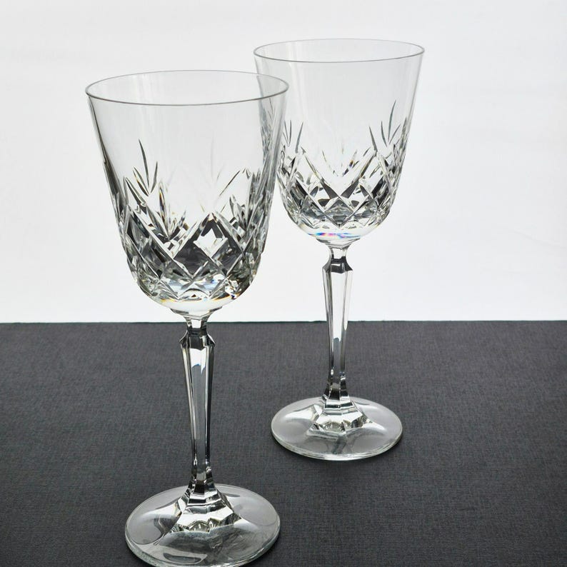K&ouml;nnte beinhalten: Zwei klare Kristall-Weingl&auml;ser mit Diamant- und vertikalen Linienmustern. Die Gl&auml;ser haben lange Stiele und runde Basen. Der Hintergrund ist ein neutrales Grau und Wei&szlig;.