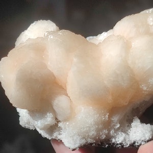 Könnte beinhalten: Ein Cluster aus orangefarbenen und weißen Calcitkristallen, die eine einzigartige und zarte Form bilden. Die Kristalle sind durchscheinend und haben eine glatte, polierte Oberfläche.