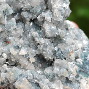 May include: A cluster of clear, sparkling crystals with a light blue, green, and grey base. The crystals are arranged in a random, natural pattern.