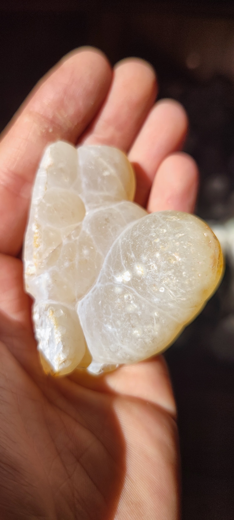 Może przedstawiać: Biały agat w kształcie serca o gładkiej, wypolerowanej powierzchni. Kamień ma naturalny, organiczny wz&oacute;r białych i jasnobrązowych żyłek.