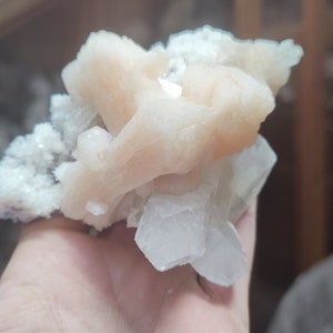 Könnte beinhalten: Ein Cluster aus rosa und weißen Cölestin-Kristallen. Die Kristalle sind durchscheinend und haben ein zartes, geschichtetes Aussehen.