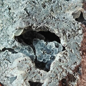 May include: A close-up of a gray and black rock with a cavity filled with small, blue crystals.