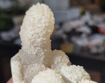 May include: A white crystal cluster with a unique, spiky formation. The crystal is translucent and has a rough, textured surface.