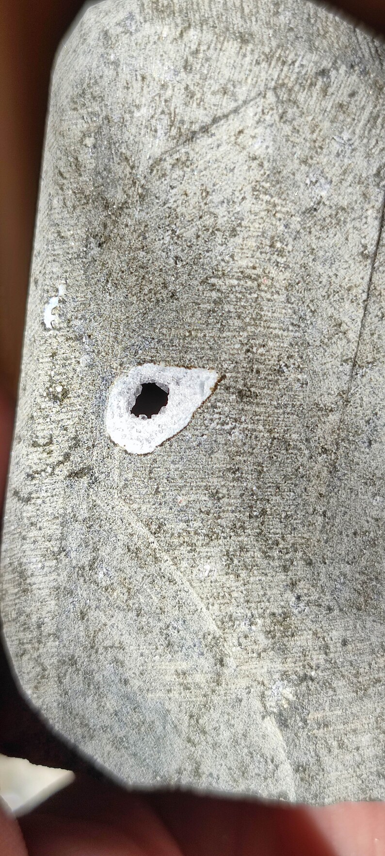 K&ouml;nnte beinhalten: Nahaufnahme einer grauen, strukturierten Oberfl&auml;che mit einem kleinen, runden Loch. Das Loch ist von einem wei&szlig;en Ring umgeben.