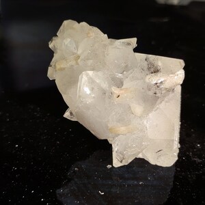 May include: A cluster of clear quartz crystals with a rough, natural texture. The crystals are arranged in a random, organic pattern, creating a unique and interesting display.