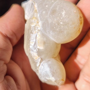 Może przedstawiać: Biała geoda agatowa o gładkim, zaokrąglonym zewnętrzu i szorstkim, teksturowanym wnętrzu. Geoda jest przezroczysta i ma mlecznobiały kolor.