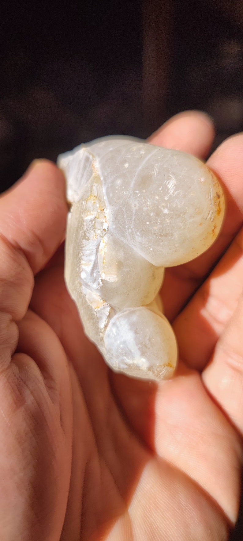 Może przedstawiać: Biała geoda agatowa o gładkim, zaokrąglonym zewnętrzu i szorstkim, teksturowanym wnętrzu. Geoda jest przezroczysta i ma mlecznobiały kolor.