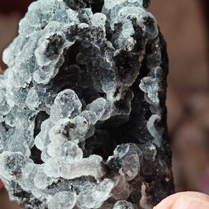 May include: A close-up of a gray and black crystal cluster with a rough, textured surface. The crystal has a unique, bubbly appearance.