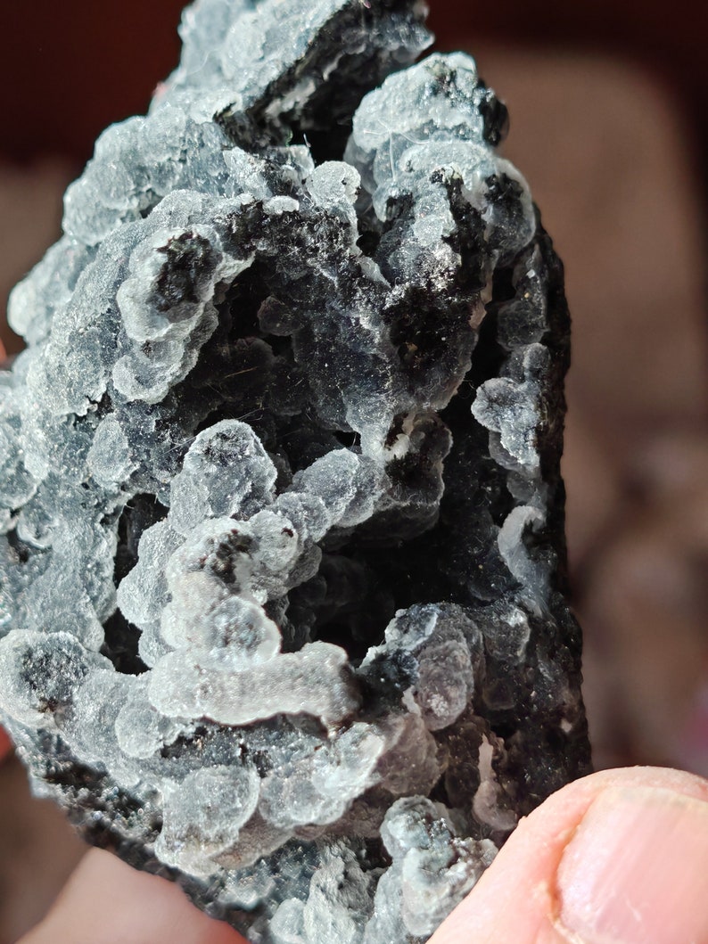May include: A close-up of a gray and black crystal cluster with a rough, textured surface. The crystal has a unique, bubbly appearance.