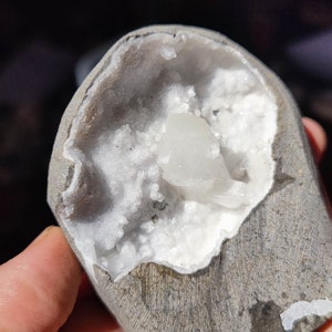 Könnte beinhalten: Ein grauer Stein mit einer Höhle, die mit weißen Kristallen gefüllt ist. Die Kristalle sind zusammengedrängt und haben ein glitzerndes Aussehen.