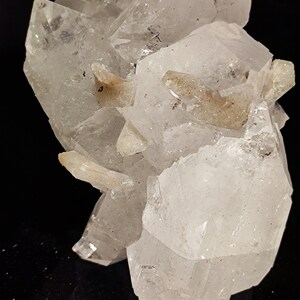 May include: A cluster of clear quartz crystals with a few brown inclusions. The crystals are arranged in a cluster, with some of the crystals pointing upwards and others pointing downwards. The crystals are translucent and have a glassy luster.