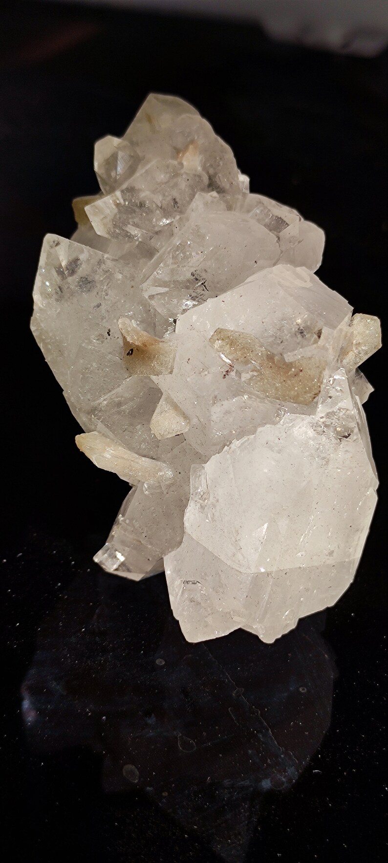 May include: A cluster of clear quartz crystals with a few brown inclusions. The crystals are arranged in a cluster, with some of the crystals pointing upwards and others pointing downwards. The crystals are translucent and have a glassy luster.