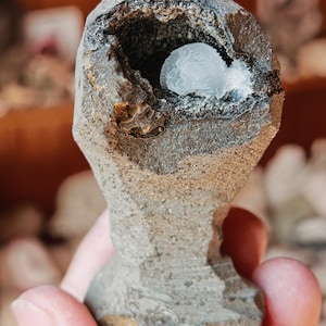 May include: A grey, irregularly shaped rock with a cavity containing a white, crystalline mineral. The rock has a rough, textured surface.