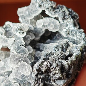 May include: A close-up of a gray and white crystal formation with a rough, textured surface. The crystal has a cluster of small, clear, bubble-like formations.