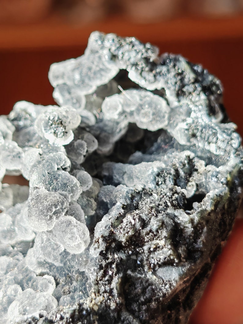May include: A close-up of a gray and white crystal formation with a rough, textured surface. The crystal has a cluster of small, clear, bubble-like formations.