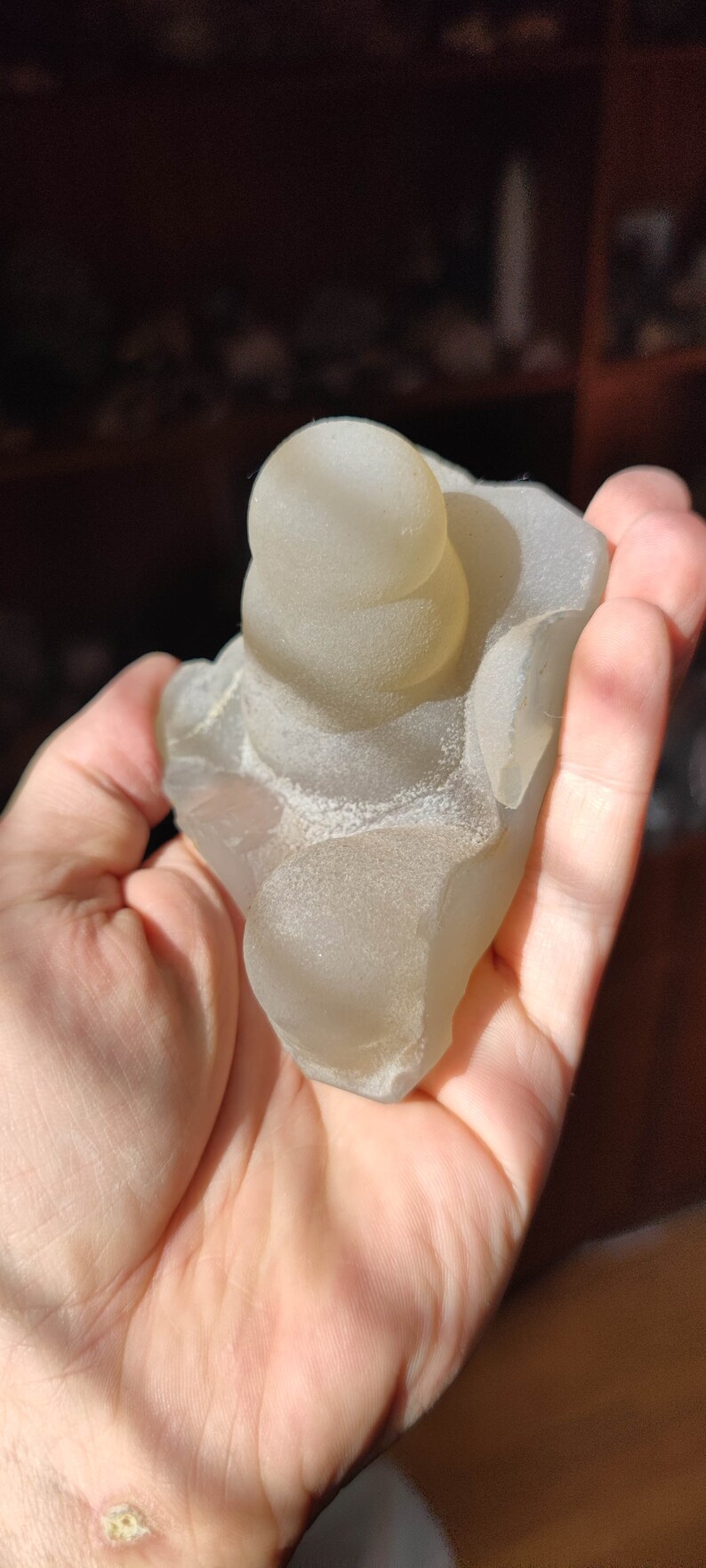 May include: A translucent, light gray, agate geode with a stacked, rounded, smooth, top formation. The geode is in the palm of a hand.