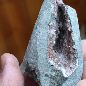 Könnte beinhalten: Ein grauer Stein mit einer natürlichen Höhle, die mit weißen und rosa Kristallen gefüllt ist. Die Kristalle sind zusammengedrängt und haben ein glitzerndes Aussehen.