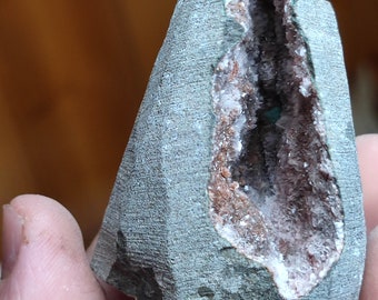 May include: A gray rock with a natural cavity filled with white and pink crystals. The crystals are clustered together and have a sparkly appearance.