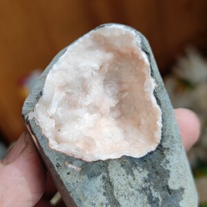 Könnte beinhalten: Ein Geode mit grauer Außenseite und einem rosa, kristallverkleideten Inneren.