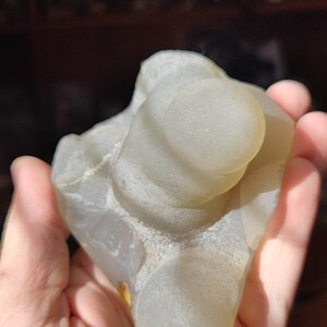 May include: A light gray agate geode with a smooth, rounded surface. The geode has several circular openings that reveal the interior of the stone.