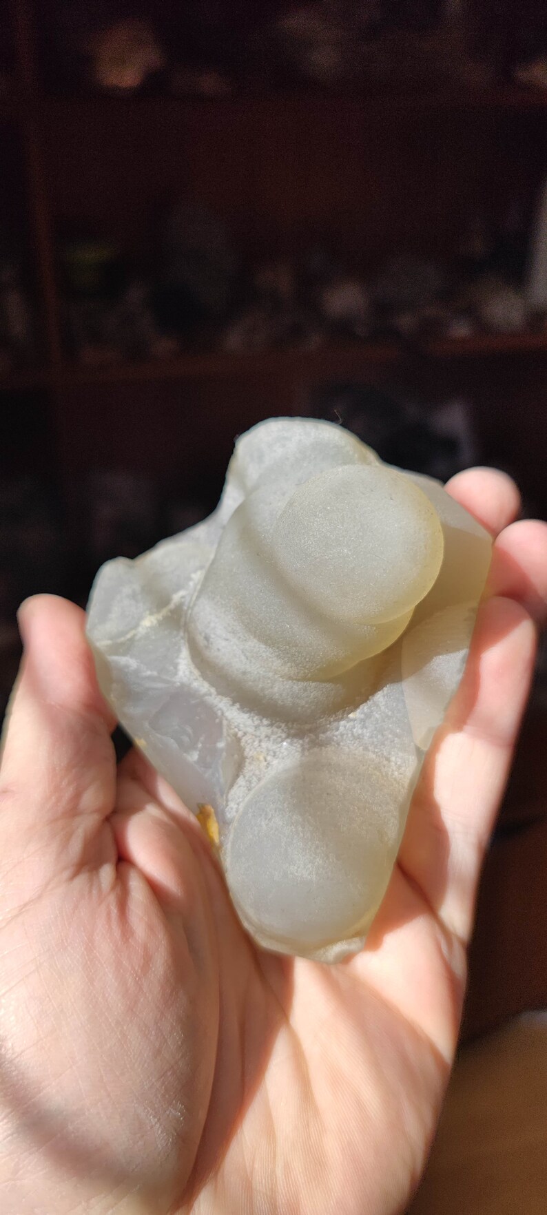 May include: A light gray agate geode with a smooth, rounded surface. The geode has several circular openings that reveal the interior of the stone.