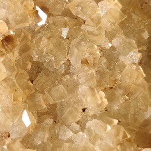 Pu&ograve; includere: Primo piano di un gruppo di piccoli cristalli traslucidi di colore marrone chiaro. I cristalli hanno una superficie ruvida e testurizzata e sono disposti in uno schema casuale.