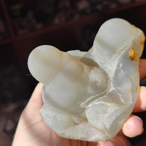 May include: A white agate geode with a smooth, rounded surface and a light brown interior. The geode is a natural formation with a unique shape and texture.