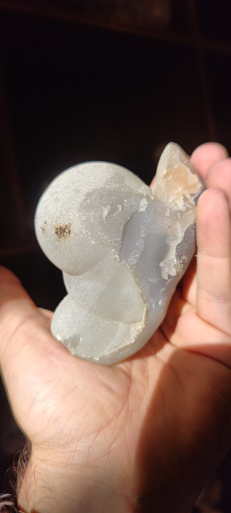 Peut inclure: Une pierre d'agate gris clair avec une surface lisse et arrondie et un bord rugueux et textur&eacute;. La pierre a une forme naturelle et organique et une qualit&eacute; subtile et translucide.