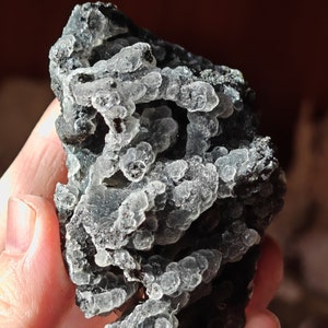 May include: A close-up of a dark gray and green chalcedony geode with a rough, textured surface. The geode is filled with small, white, translucent crystals.