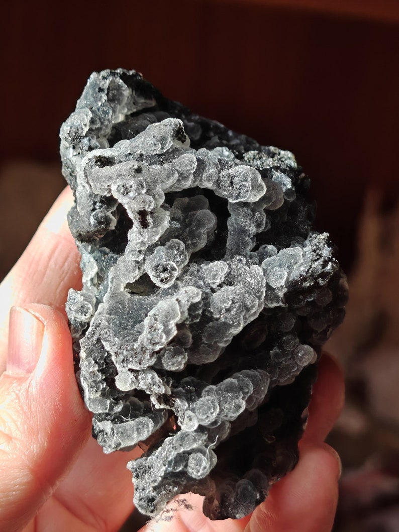 May include: A close-up of a dark gray and green chalcedony geode with a rough, textured surface. The geode is filled with small, white, translucent crystals.