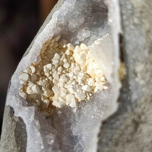 K&ouml;nnte beinhalten: Nahaufnahme einer Geode mit einem wei&szlig;en, kristallinen Inneren. Die Geode ist teilweise ge&ouml;ffnet und zeigt einen Cluster aus kleinen, wei&szlig;en Kristallen.