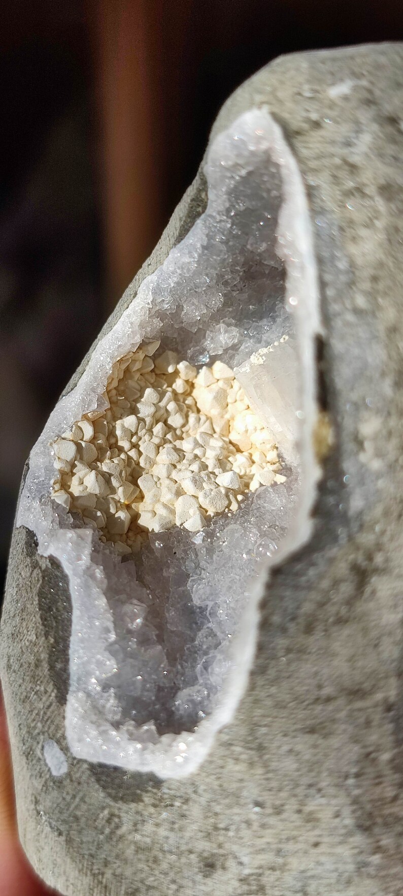 K&ouml;nnte beinhalten: Nahaufnahme einer Geode mit einem wei&szlig;en, kristallinen Inneren. Die Geode ist teilweise ge&ouml;ffnet und zeigt einen Cluster aus kleinen, wei&szlig;en Kristallen.
