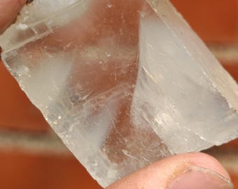 May include: A clear, translucent crystal with a slightly cloudy appearance. The crystal has a geometric shape with sharp edges and flat surfaces.
