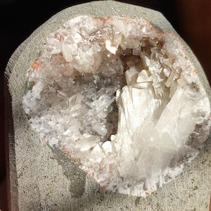 Könnte beinhalten: Ein grauer Stein mit einer hohlen Mitte, die mit weißen Kristallen gefüllt ist. Die Kristalle sind zusammengedrängt und haben ein glänzendes, durchscheinendes Aussehen.