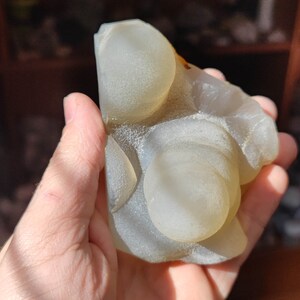 May include: A white agate geode with a smooth, rounded surface and a light brown rim. The geode has several round, translucent orbs inside.