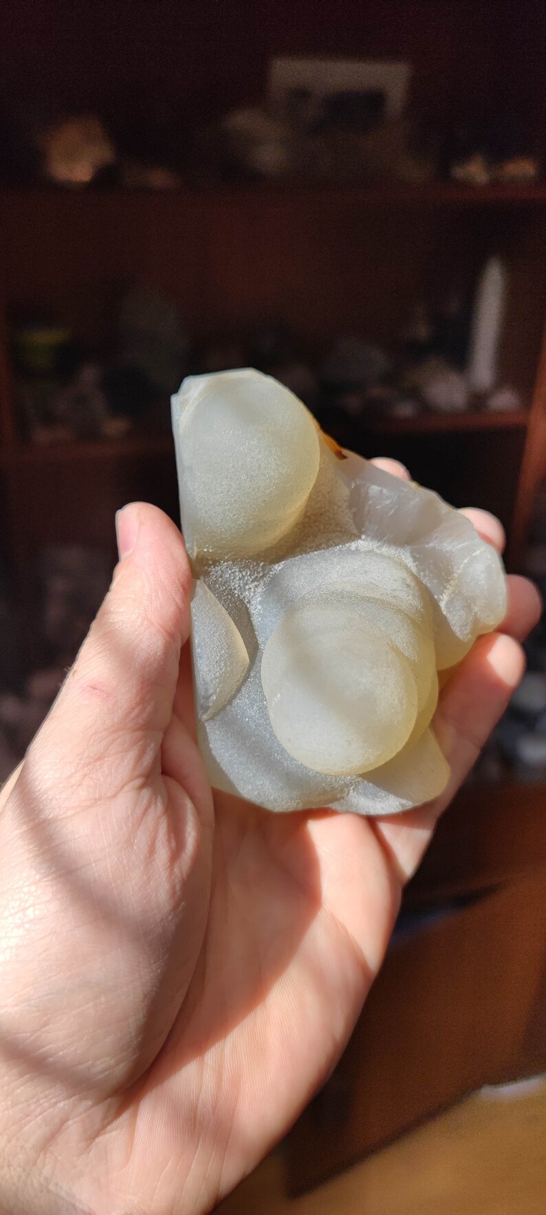 May include: A white agate geode with a smooth, rounded surface and a light brown rim. The geode has several round, translucent orbs inside.