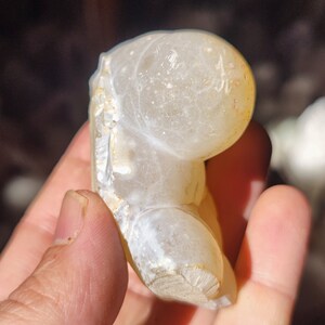 Może przedstawiać: Biała geoda agatowa o gładkiej, zaokrąglonej powierzchni i naturalnej, szorstkiej fakturze. Geoda ma jasnobrązowy kolor na krawędziach i białe wnętrze.