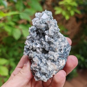 May include: A cluster of light grey and white crystals with a green and grey base. The crystals are clustered together in a rough, natural formation.