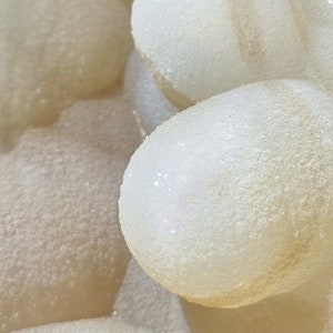 May include: Close-up of a white, textured, agate geode with a smooth, rounded interior. The geode is filled with small, white crystals.