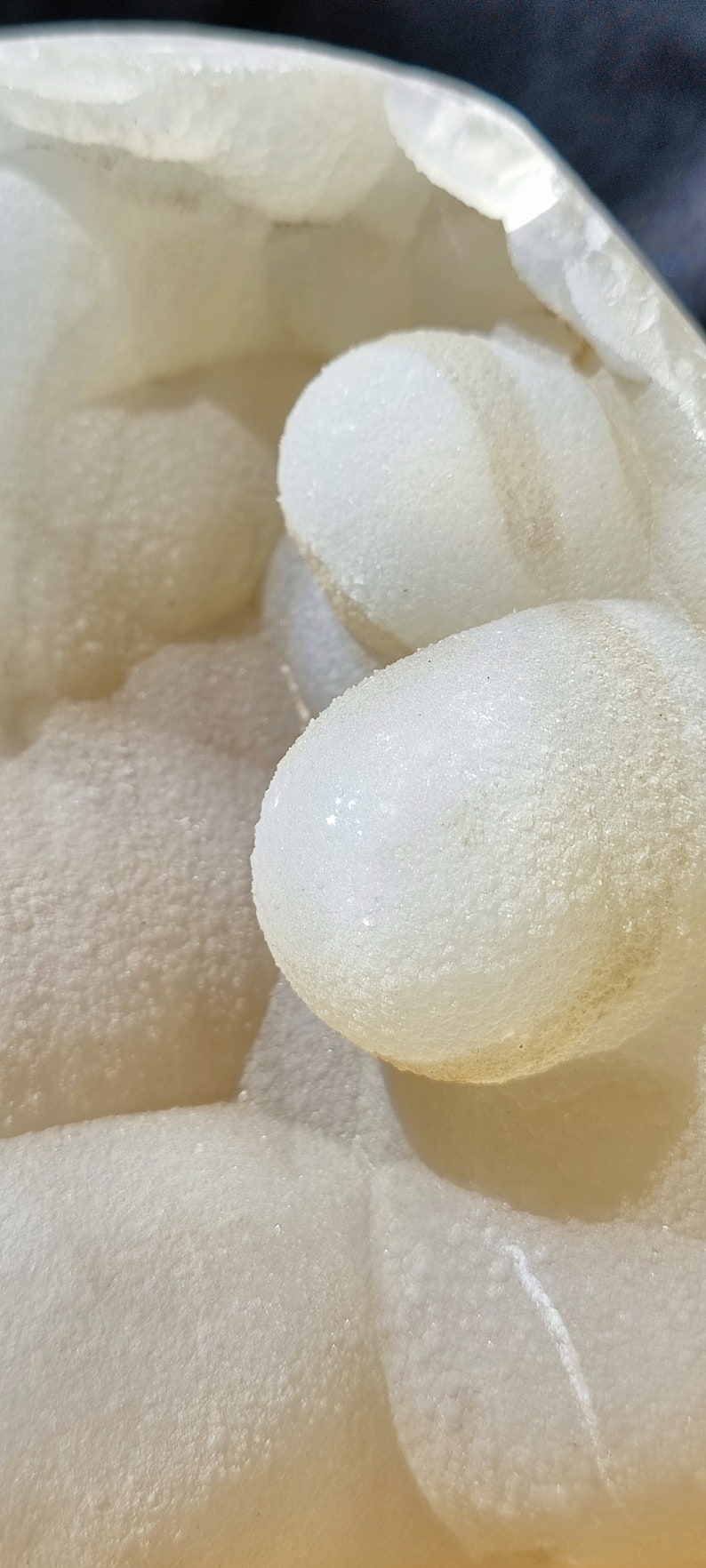 May include: Close-up of a white, textured, agate geode with a smooth, rounded interior. The geode is filled with small, white crystals.