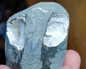 May include: A gray rock with a white, crystalline interior. The rock has a rough, textured surface and is held in a hand.