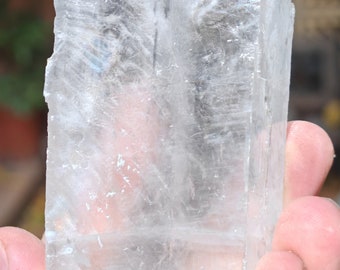 May include: A clear, translucent crystal with a rectangular shape. The crystal has a smooth, polished surface and appears to be made of selenite.