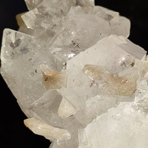 May include: A cluster of clear quartz crystals with a few smaller, opaque crystals. The crystals are arranged in a cluster, with some of the crystals pointing upwards and others pointing downwards.
