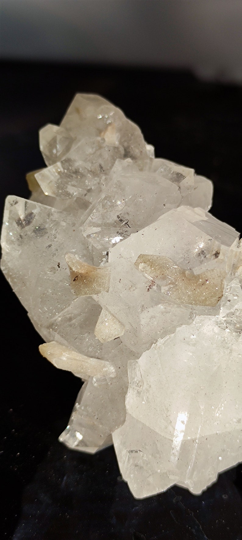 May include: A cluster of clear quartz crystals with a few smaller, opaque crystals. The crystals are arranged in a cluster, with some of the crystals pointing upwards and others pointing downwards.