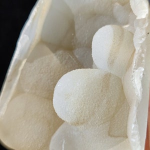 May include: A white geode with a cluster of small, round, white crystals inside. The geode is open and the crystals are visible.