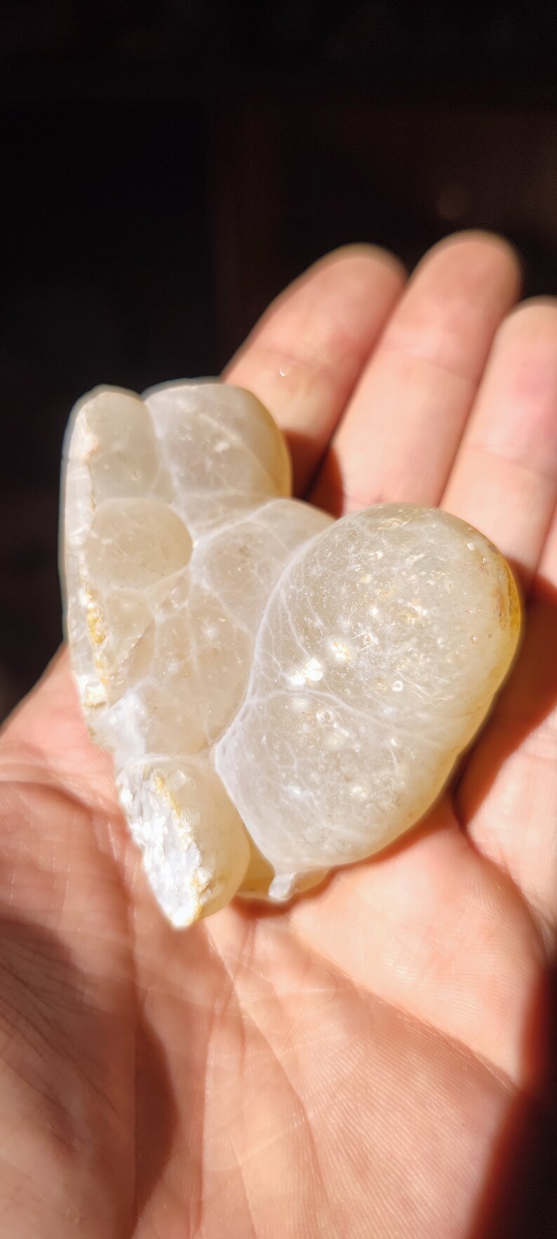 Może przedstawiać: Biały agat o unikalnym, organicznym kształcie i gładkiej, wypolerowanej powierzchni. Kamień jest prześwitujący i ma skomplikowane wzory w kolorze białym i szarym.