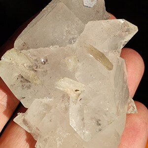 May include: A cluster of clear quartz crystals with a slightly cloudy appearance. The crystals are clustered together in a natural formation.